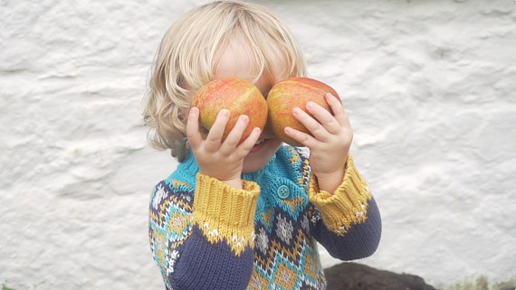 child holding up apples to his eyes wearing a jumper