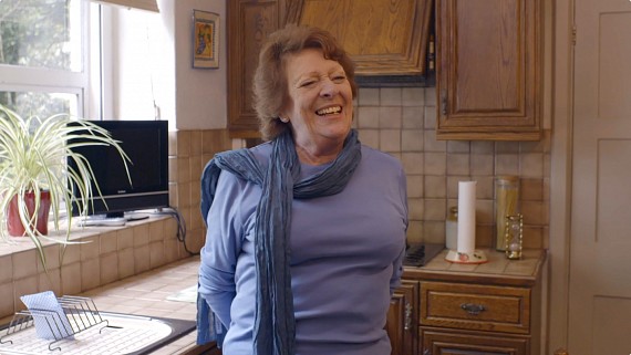 Woman standing in a kitchen smiling off camera