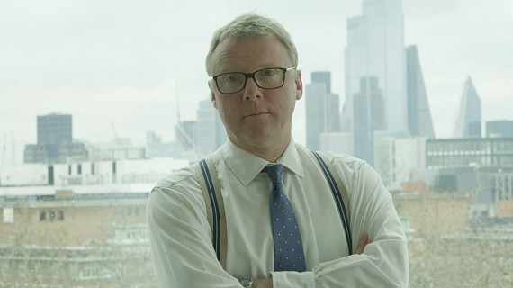 Business man wearing shirt tie and braces folding arms in front of london cityscape window