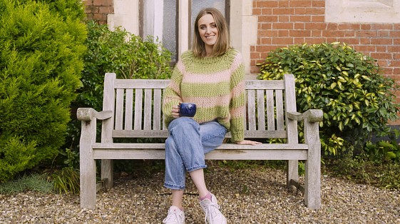 girl sitting on park bench smiling with cup of tea