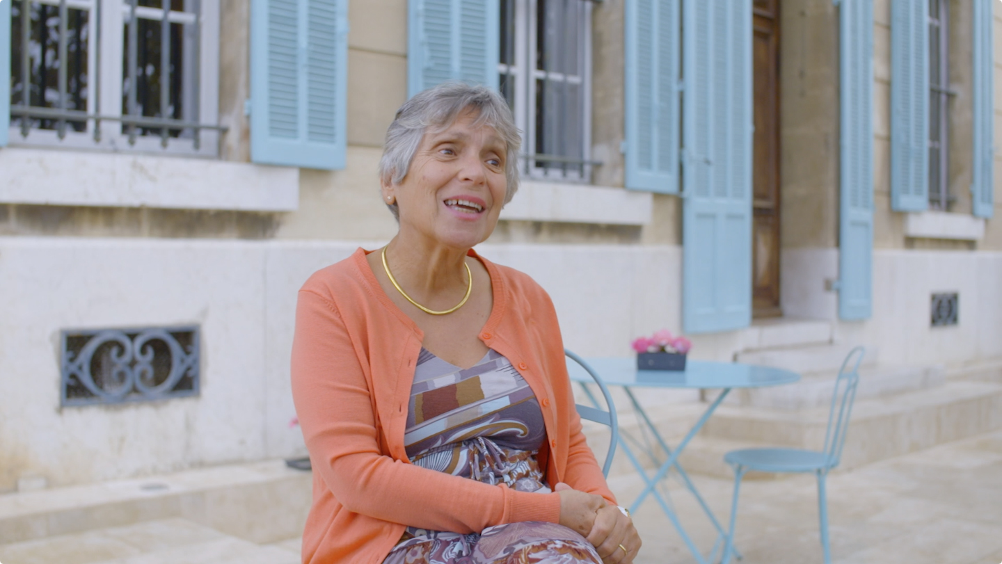 Woman seated outside a property with blue shutters in France, from MHF Creative's Expedia customer story campaign.