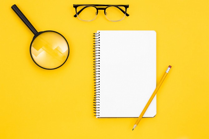 Magnifying glass notebook and glasses yellow background