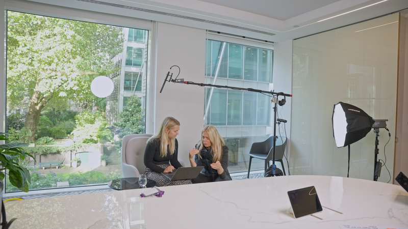 Behind-the-scenes of recruitment video production at Evelyn Partners, showing two female leaders discussing at a laptop with full filming setup, capturing authentic leadership stories.