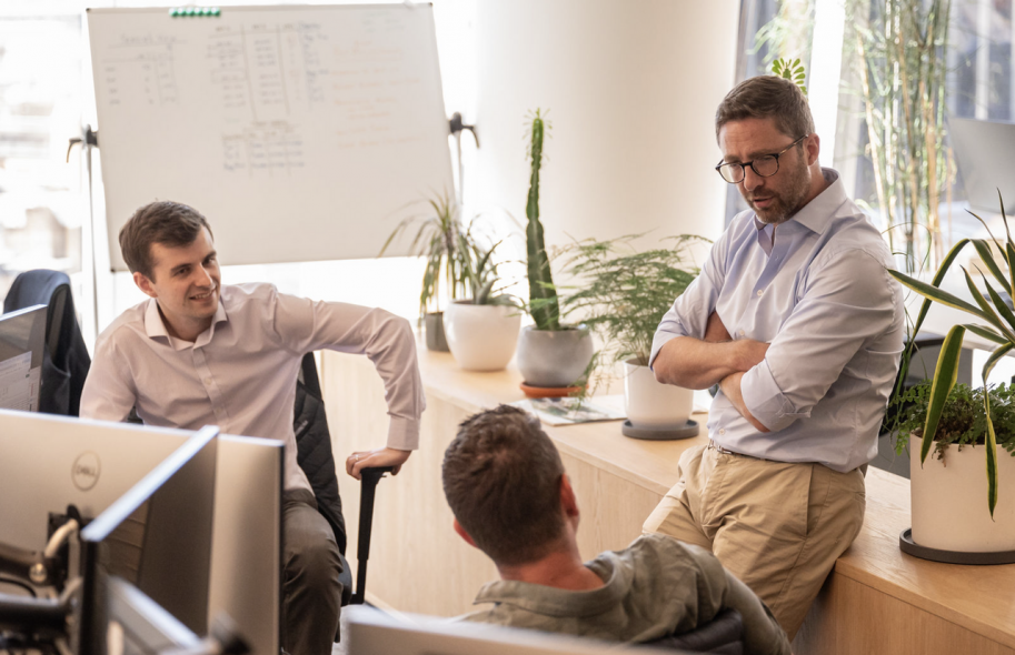 Candid team discussion in a modern office environment, captured for a recruitment video showcasing authentic workplace culture and collaboration.