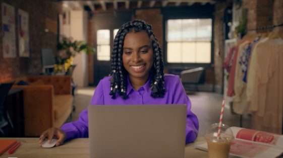Digital marketer persona smiling while working on a laptop in a bright, modern workspace.