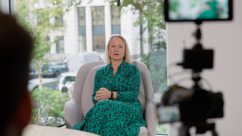 Female wearing green dress sitting talking to video production crew in front of window