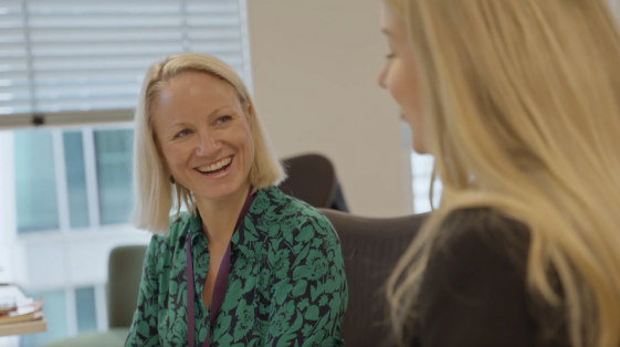 blonde female smiling at another colleague sitting at desk