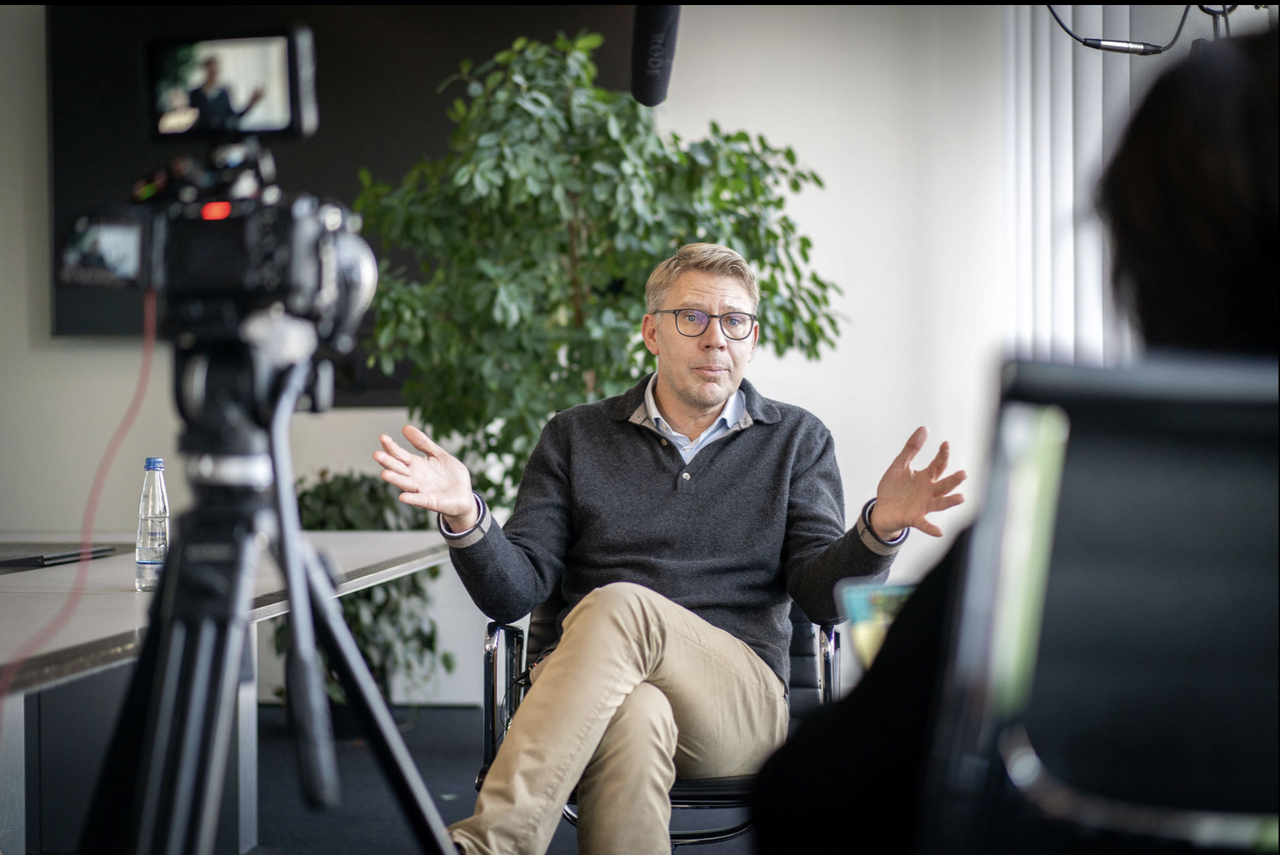 Video production crew filming an executive interview in a modern office setting, with camera and boom microphone visible.