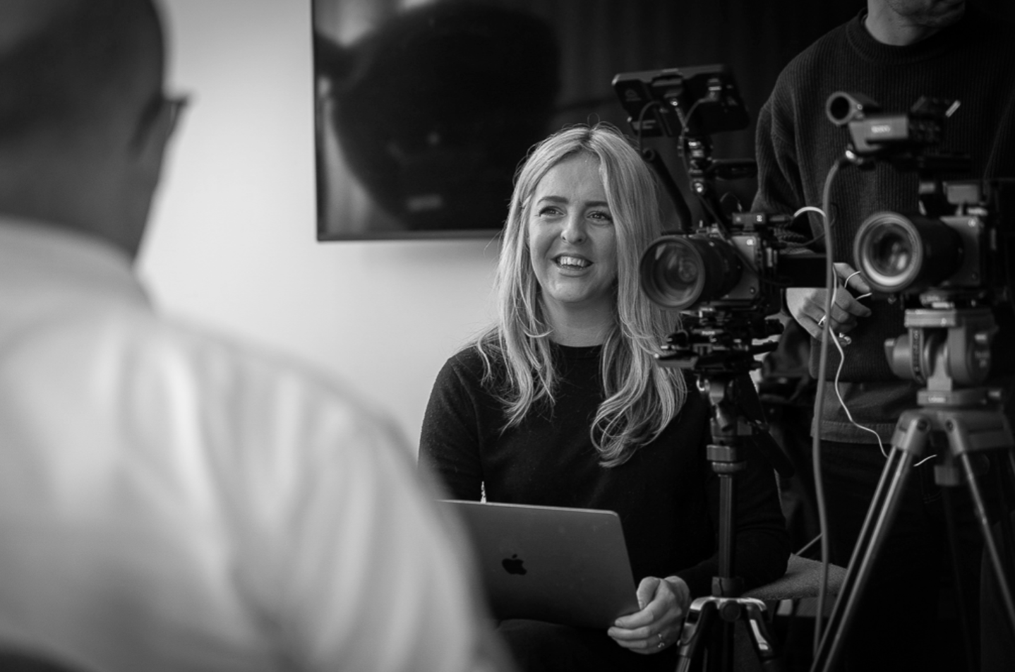 Video producer listening and smiling during an on-camera interview, with filming equipment set up beside her.